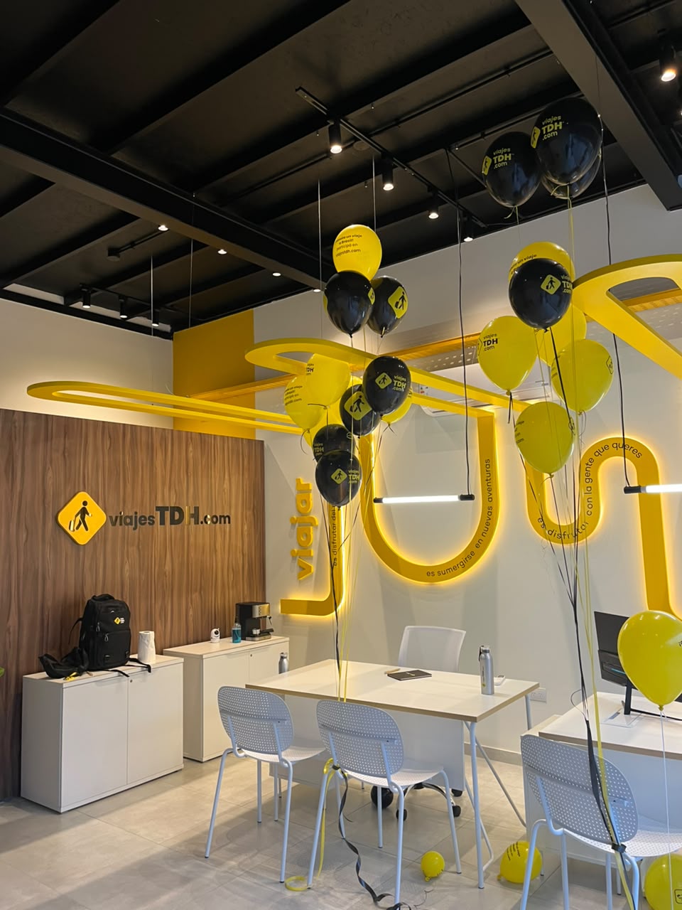 Interior de un local Viajes TDH recién inaugurado, con la faja amarilla iluminada y globos de la marca